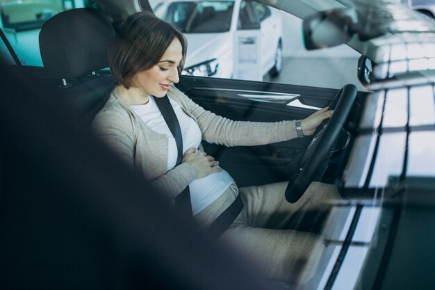 Mujer embarazada joven que prueba un coche en la sala de exposición de automóviles