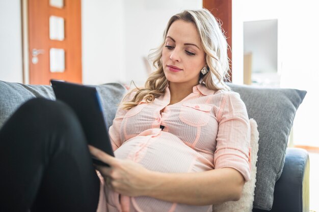 Mujer embarazada joven relajada que usa la tableta digital