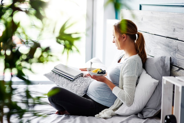 Mujer embarazada leyendo un libro en el dormitorio