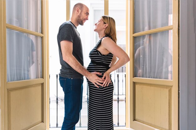 Mujer embarazada y marido enfrente de ventanas abiertas