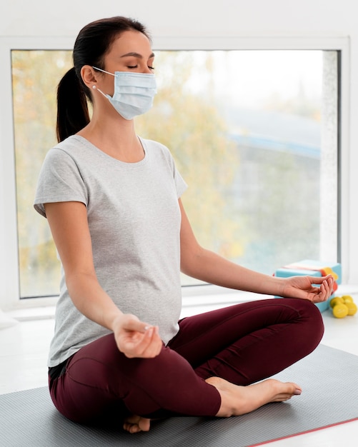 Mujer embarazada con máscara médica haciendo yoga