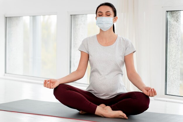 Mujer embarazada con máscara médica meditando