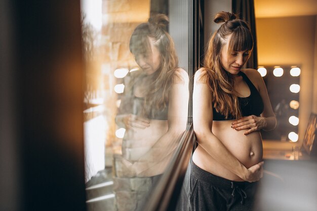 Mujer embarazada de pie junto a la ventana