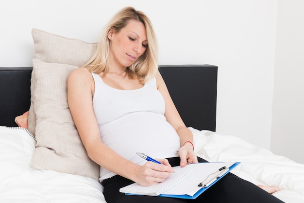 Mujer embarazada con portapapeles en cama
