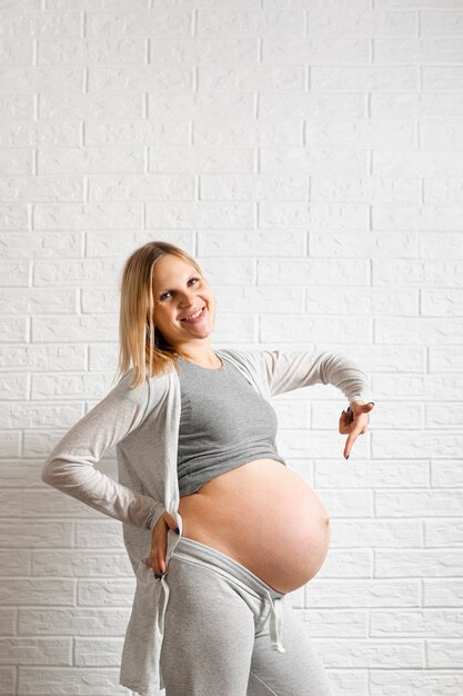 Mujer embarazada posando delante de una pared y apuntando a su vientre