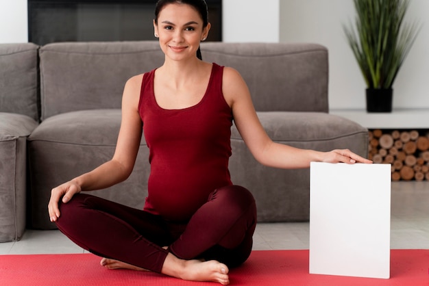 Mujer embarazada posando junto a la tarjeta blanca
