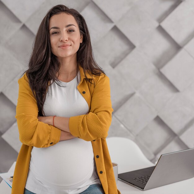 Mujer embarazada posando con portátil y hogar