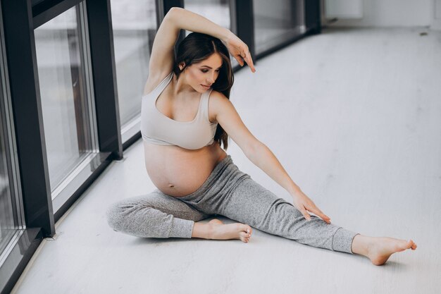 Mujer embarazada practicando yoga en casa junto a la ventana