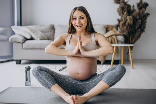 Mujer embarazada practicando yoga en estera en casa