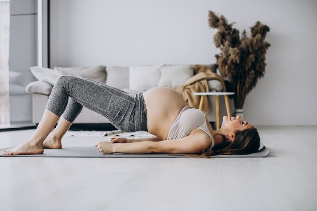 Mujer embarazada practicando yoga en estera en casa