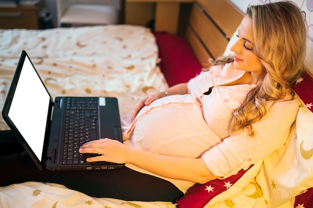 Foto gratuita mujer embarazada que usa la computadora portátil con la pantalla blanca en blanco