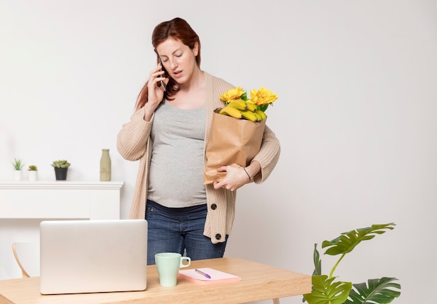 Mujer embarazada con ramo de flores hablando por teléfono