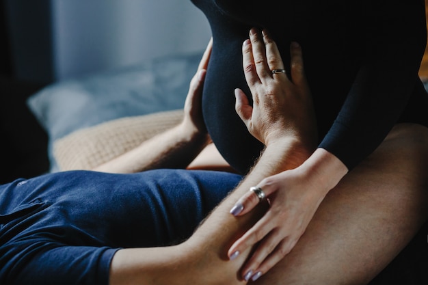 La mujer embarazada se sienta sobre su marido, y él le toma las manos sobre el vientre.