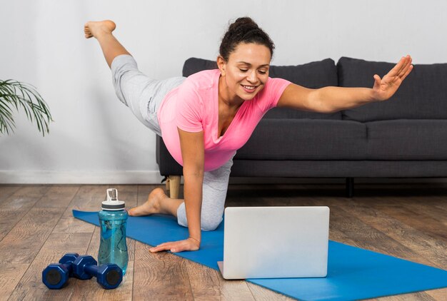 Mujer embarazada sonriente en casa ejercicio de yoga con portátil