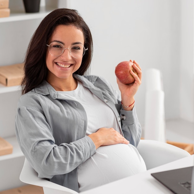 Mujer embarazada sonriente en casa sosteniendo una manzana