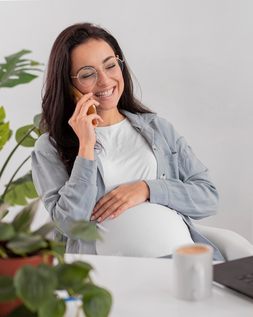 Foto gratuita mujer embarazada sonriente hablando por teléfono mientras trabaja