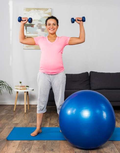 Mujer embarazada sonriente haciendo ejercicio en casa con pesas y pelota