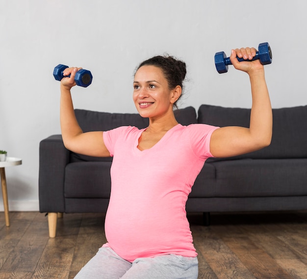 Foto gratuita mujer embarazada sonriente haciendo ejercicio con pesas