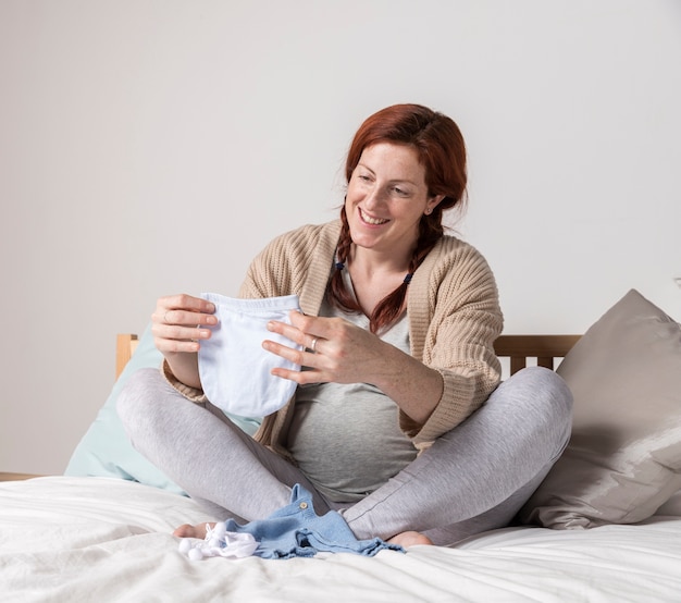 Foto gratuita mujer embarazada sonriente mirando ropa de bebé