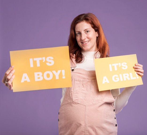 Mujer embarazada sonriente que sostiene el papel con género del bebé