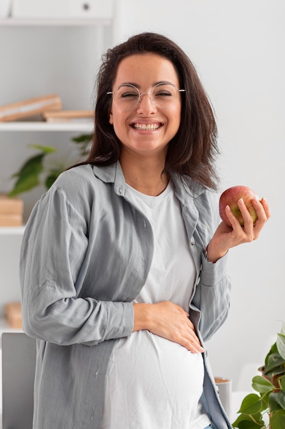 Mujer embarazada sonriente sosteniendo una manzana en casa