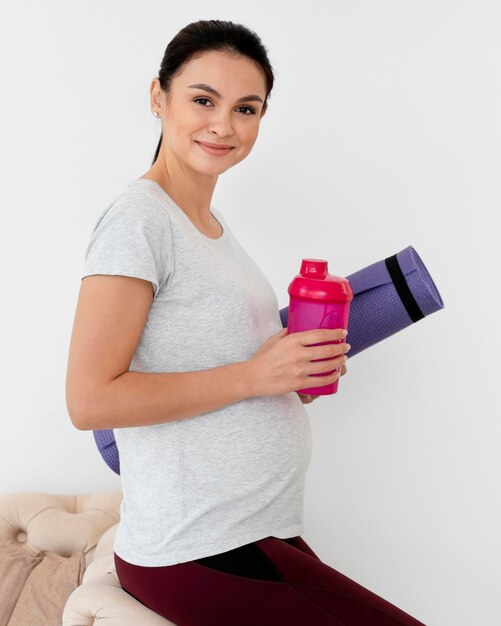 Mujer embarazada sosteniendo una colchoneta de fitness y una botella de agua