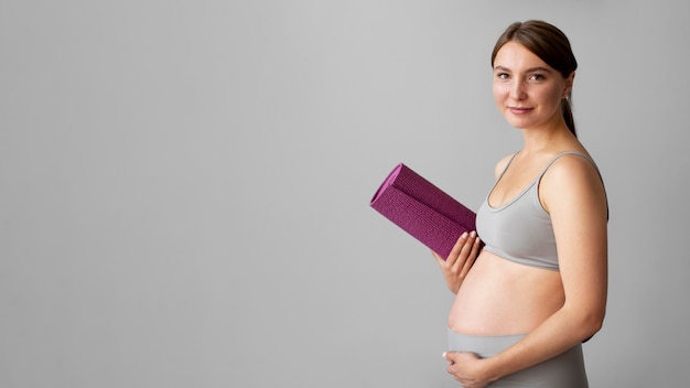 Mujer embarazada sosteniendo una colchoneta de fitness con espacio de copia