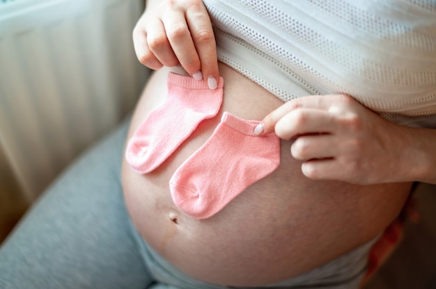 Mujer embarazada sosteniendo pequeños calcetines en su vientre desnudo