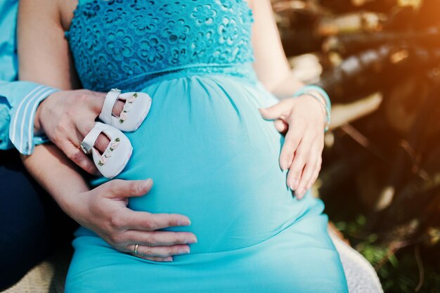 Mujer embarazada y su esposo cogidos de la mano en la barriga con zapatos de bebé para niñas Nuevo tema de vida