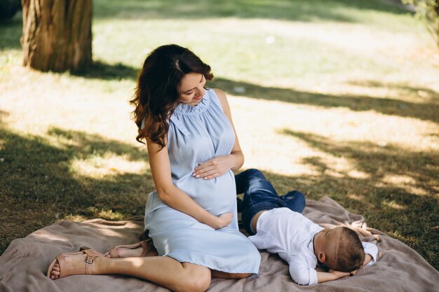 Mujer embarazada y su pequeño hijo que tienen comida campestre en parque