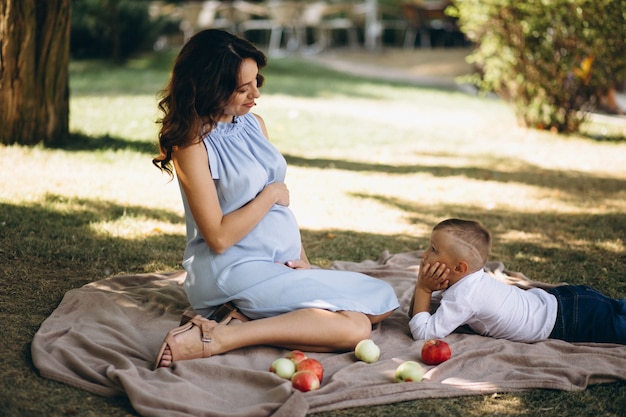 Mujer embarazada y su pequeño hijo que tienen comida campestre en parque