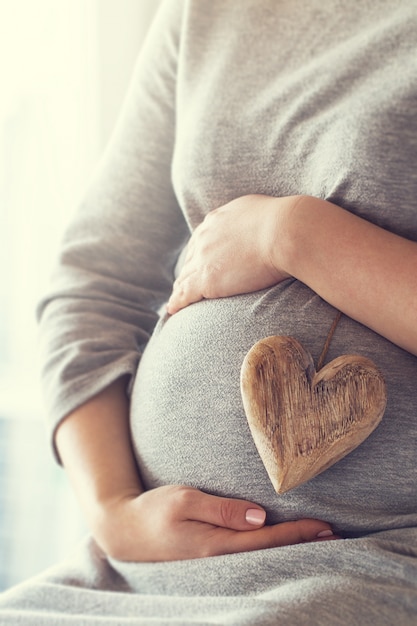 Mujer embarazada sujetando un corazón mientras se toca la barriga