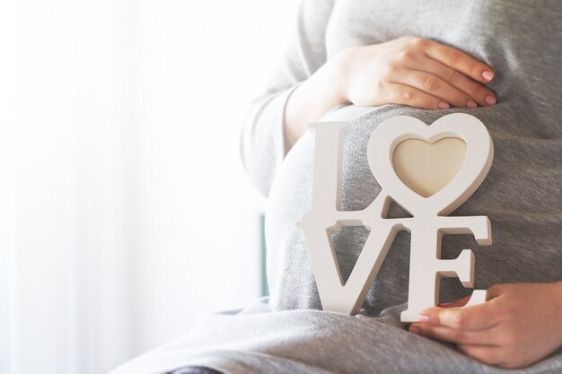 Mujer embarazada sujetando la palabra "love"