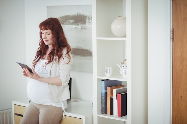 Mujer embarazada con tableta digital en la sala de estudio
