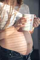 Foto gratuita una mujer embarazada con una taza de té en la ventana por la mañana.