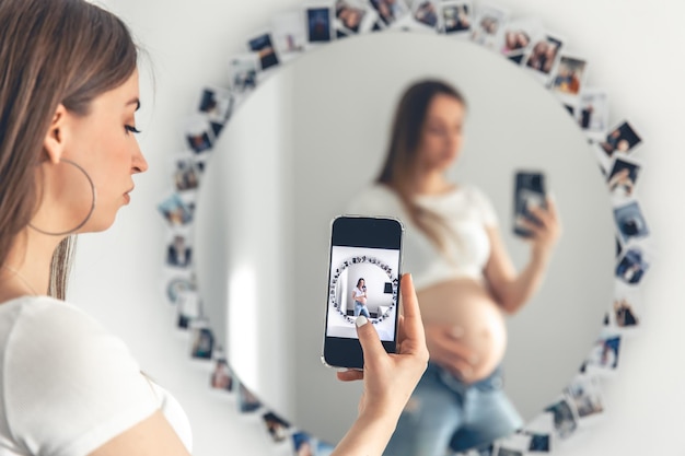 Foto gratuita una mujer embarazada se toma una selfie en el espejo el concepto de esperar un bebé