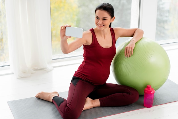 Mujer embarazada tomando un selfie junto a una pelota de fitness