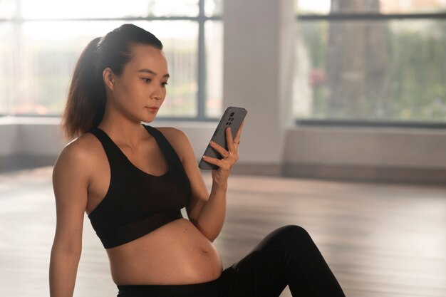Mujer embarazada usando un teléfono inteligente mientras hace yoga