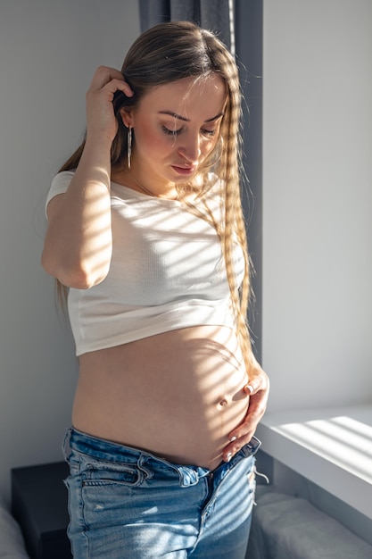 Foto gratuita una mujer embarazada en la ventana en una mañana soleada