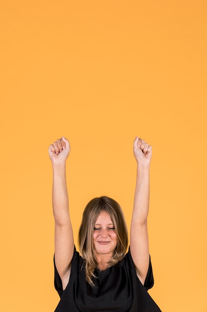 Foto gratuita mujer emocionada bombeando puños con los ojos cerrados sobre fondo amarillo