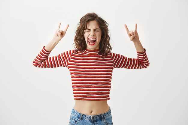 Mujer emocionada despreocupada sonriendo y mostrando gesto de rock-n-roll