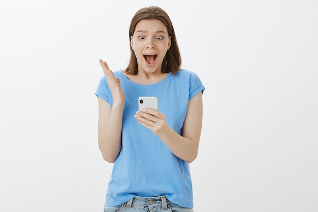 Mujer emocionada gritando de asombro y mirando la pantalla del teléfono inteligente