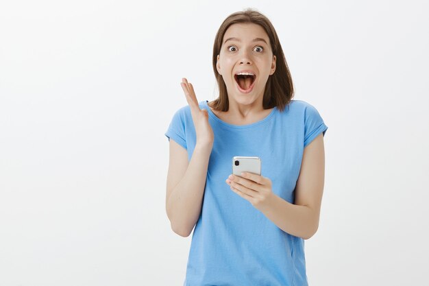 Mujer emocionada gritando de asombro y mirando la pantalla del teléfono inteligente