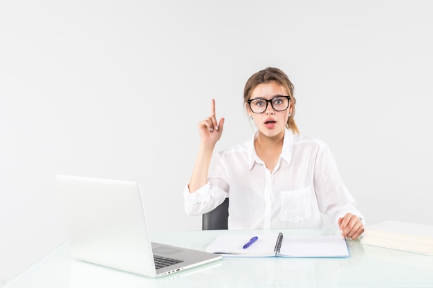 La mujer emocionada joven en ropa en colores pastel que levanta el dedo índice con gran idea nueva se sienta, trabaja en el escritorio con la computadora portátil aislada en fondo gris. Logro concepto de carrera empresarial.