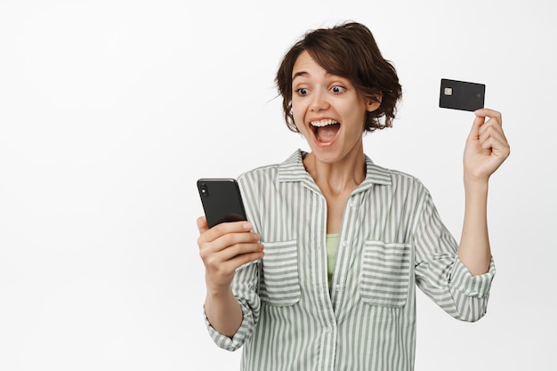 Mujer emocionada mirando el teléfono móvil y levantando la tarjeta de crédito.