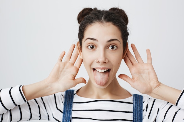 Foto gratuita mujer emocionada muestra la lengua, toma las manos cerca de los oídos, escucha