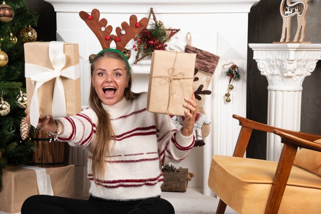 Una mujer emocionada en orejas de ciervo con dos regalos de Navidad.