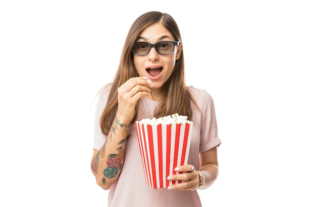 Mujer emocionada con palomitas de maíz mientras ve una película en 3D sobre fondo blanco.