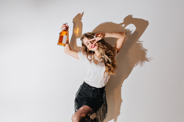 Foto gratuita mujer emocionada con peinado rizado bailando con botella de coñac