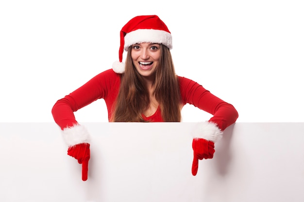 Foto gratuita mujer emocionada con sombrero de santa mostrando en cartelera en blanco